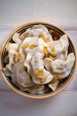 Pierogi or pyrohy, varenyky, vareniki, dumplings in bowl on wooden table. vertical