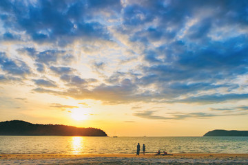 Pantai Tengah Beach at colorful sunset, Langkawi Island, Malaysia. Beach sunset is a golden sunset sky with a wave rolling to shore as the sun sets over the horizon. People relaxing on paradise beach