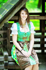 young woman wearing a dirndl sitting at wooden lodge