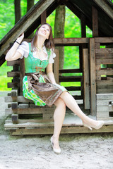 young woman wearing a dirndl sitting at wooden lodge