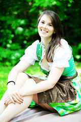 young woman in dirndl sitting on blanket in park