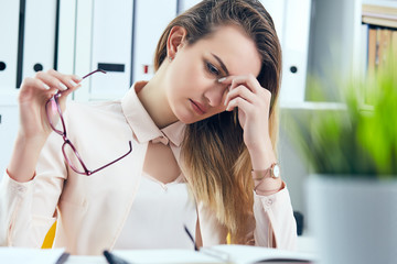 Tired overworked businesswoman in glasses at office covering her face with hand.