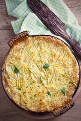 Classic homemade shepherd's pie (mashed potato and ground beef with vegetables) in casserole baking dish on wooden table. overhead, vertical