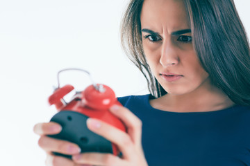 Portrait of shocked and angry woman with alarm clock over white background.