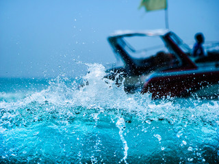 Clear blue sea wave make splashing with white bubble with blurred background of speed boat