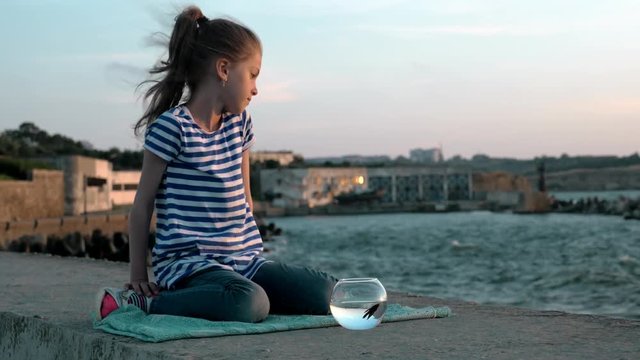 sad child girl seated on the coast with his fish a rounded aquarium outdoors in summer. concept environment