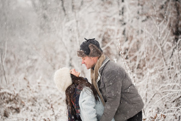 Side view of the young happy couple who is standing in embrace in the snow-covered park
