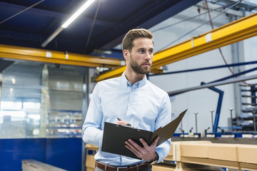 Young businessman with clipboard in production hall