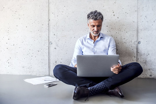 Mature businessman sitting on the floor using laptop