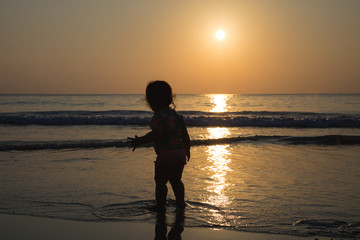 Silhouette of Happy baby girl is enjoying the golden sunset at the sand beach on the seashore somewhere in Thailand