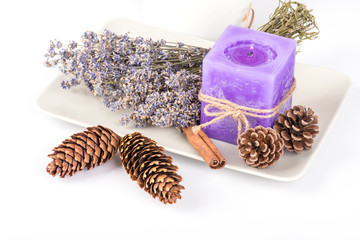 Still life with lavender candle, fir cones and dry lavender on a white plate on white background