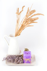 Still life with a white jug and a plate with dry lavender flowers and a lavender candle on white background
