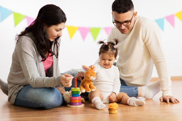 family, holidays and people concept - happy mother, father and little daughter playing with toy rabbit on birthday party