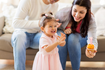 family, holidays and people concept - mother, father with cupcake and happy little daughter at home birthday party