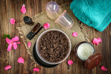 Fototapeta na wymiar Coffee body scrub, sugar and coconut oil, essential oils, massage vacuum jars on dark wooden rustic table with pink flowers. Homemade cosmetic for peeling and spa care.