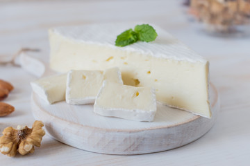 Fresh Brie cheese and a slice on a wooden board with nuts