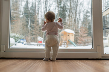 Rear view of baby girl standing in front of dirty window