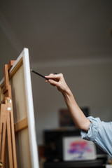 A woman paints on canvas with a brush and paints in her art studio. The frame is only a woman's hand.