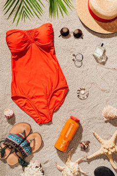 top view of stylish red swimsuit with various accessories on sandy beach