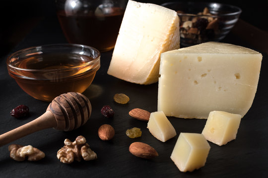 Greek cheese graviera and a slices on black stone board with nuts, honey and herbs.