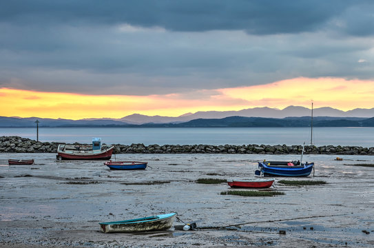 A variety of colorful little fishing boats and sloops stranded on the beach of Morecambe, Lancashire, England during sunset, with the bay of Morecambe and the mountians of Cumbria in the background