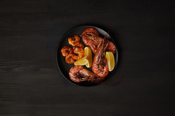 top view of grilled shrimps and lemon pieces on plate on black surface