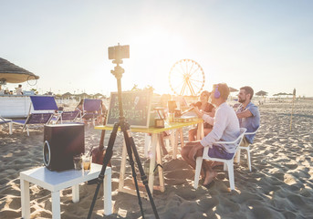 Group of young people making a video live streaming from beach party at sunset