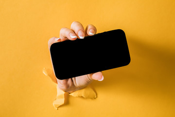 A woman holding a phone through a torn yellow paper