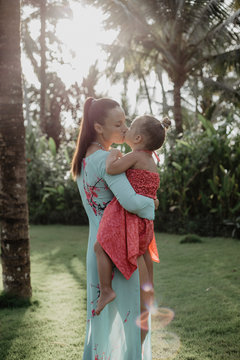 Mama und Tochter küssen sich unter Palmen mit Gegenlicht
