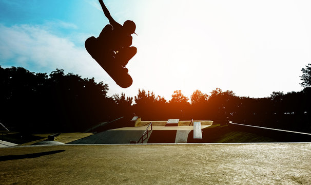 Silhouette of young skater jumping on ramp at city park - Boy performing tricks and skills with skateboard at sunset  - Youth lifestyle and extreme sport concept