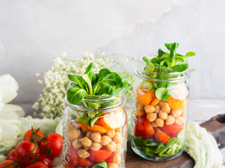 Fresh salad lunch with chickpeas, tomatoes, carrots and valerian served in mason jars