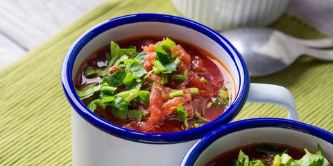 Russian beetroot soup borscht in enamel mugs on green cloth