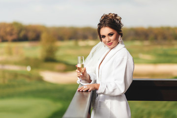 The bride is holding a glass of champagne. wedding morning. Happy and smiling girl. Outdoors