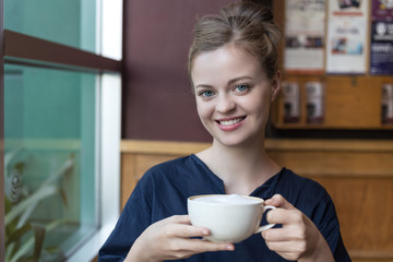 Young, smiling caucasian woman with cup of coffee in cafe