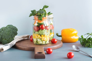 Vegetable healthy homemade colorful salad in mason jar with tomato, lettuce, broccoli on blue. Copy space. Lunch for work.
