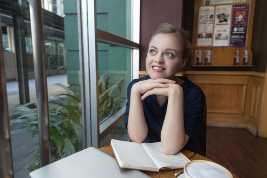 Beautiful caucasian young woman smiling and looking away, picture taken in cafe interior