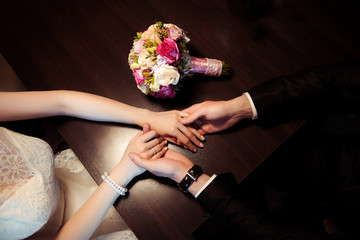 Wedding couple is sitting at the coffee table in cafe. Man touches woman's hands, bouquet of roses lies on the table. Top view