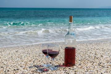 Glasses of red wine and bottle on the beach at the summer sunny day. Sea on the background.