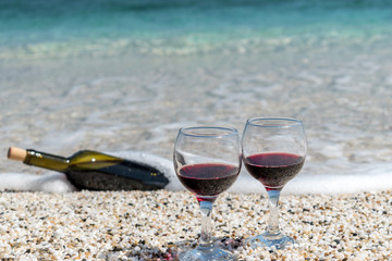 Glasses of red wine and bottle on the beach at the summer sunny day. Sea on the background.