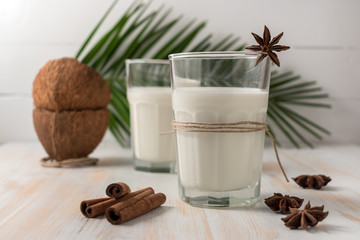 Shell of coconut and coconut milk in glass with cinnamon on wooden table.