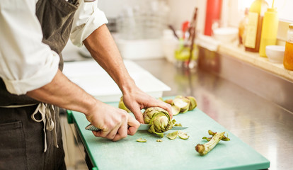 Chef cutting artichokes for dinner preparation - Man cooking inside restaurant kitchen - Focus on vegetable - Vegan cuisine, lifestyle and healthy food concept - obrazy, fototapety, plakaty