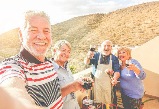 Happy senior friends taking selfie at barbecue dinner in rented villa with mountain view