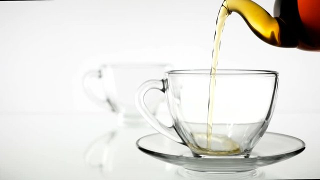 Black tea is poured into a glass beaker from a glass teapot. Slow motion. White background