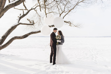 Bride and groom among snowy landscape with big white balloons. Bride and groom walk the snowy road.   Beautiful winter fairy tale, wedding card