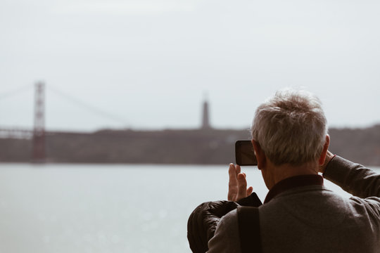 Senior Man taking picture with smart phone at the bridge in Lisbon - Portugal.
