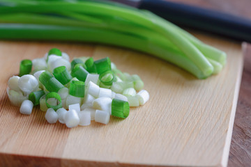 Close up view on chopped fresh spring onion and knife put on wood cutting board on wooden table with copy space. Prepare scallions for cooking. Food and vegetable concept for background or wallpaper.
