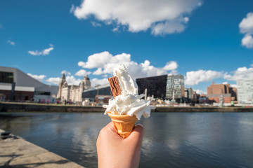 Hand holding ice cream cone with blurred image of the building at Liverpool Waterfront near Albert...