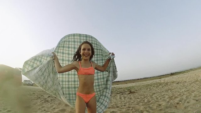 Little girl playing with the wind on the beach using a piece of tablecloth as a paraglide.