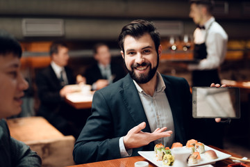 Meeting with chinese businessmen in restaurant. Man is showing tablet.
