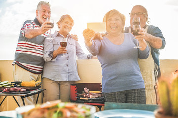 Happy seniors friends taking a selfie photo with smartphone camera at barbecue dinner in house terrace